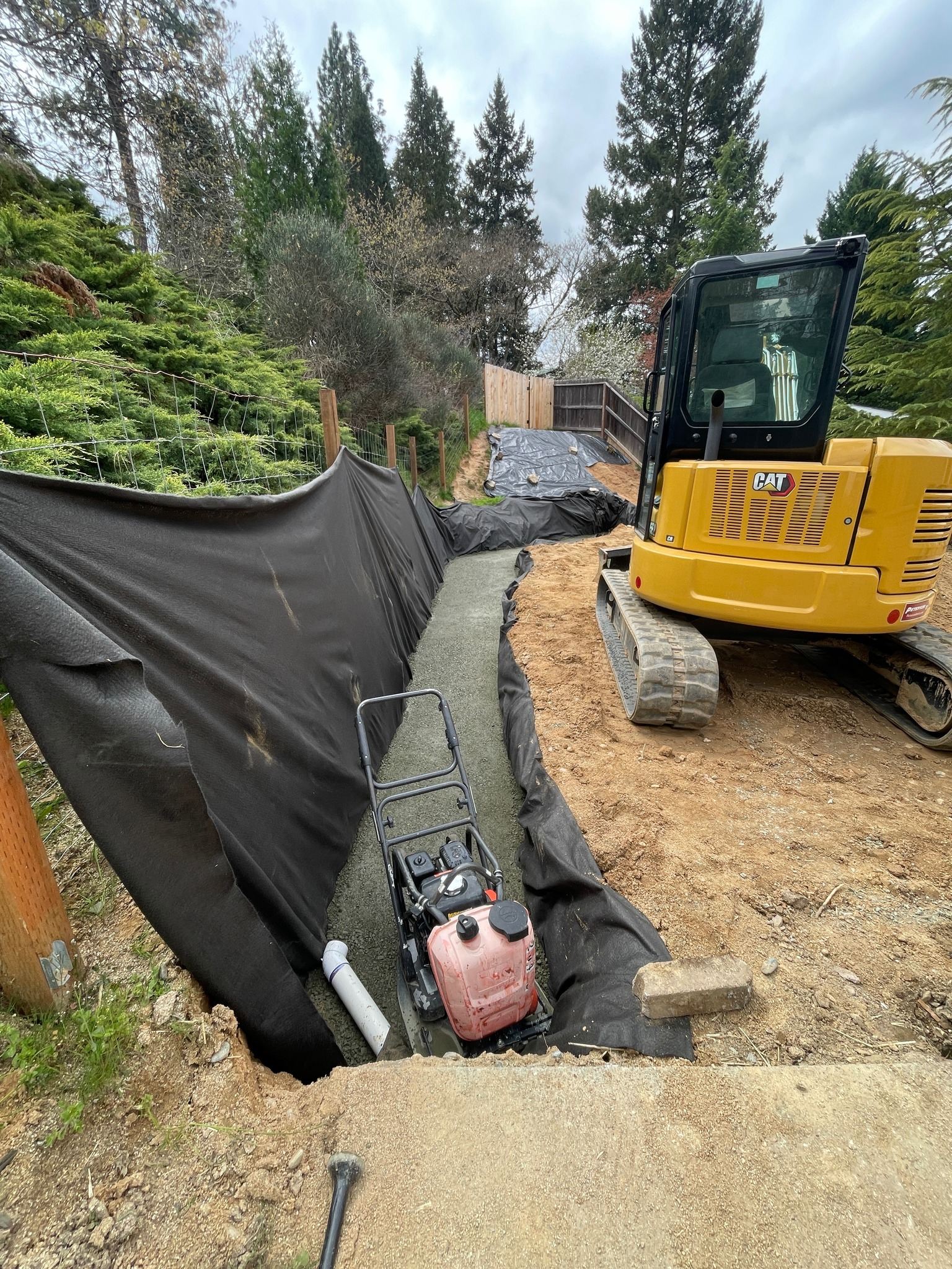 Hillside drainage trench with compactor and CAT excavator during an erosion control installation in Southern Oregon