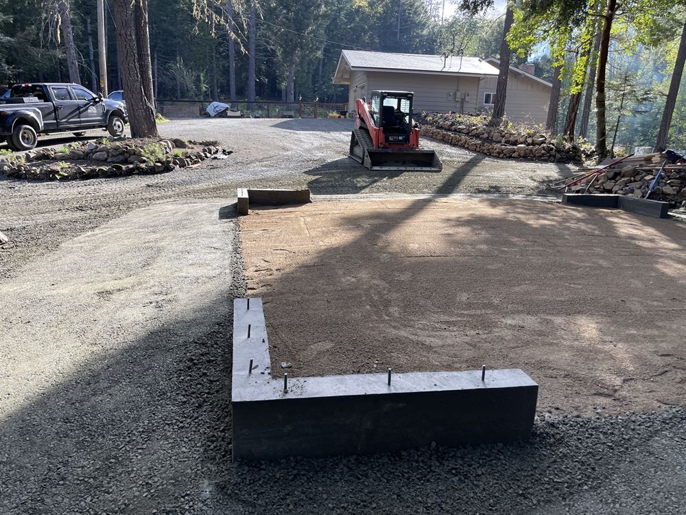 Skid steer grading a gravel driveway and building pad on a forested Rogue Valley property