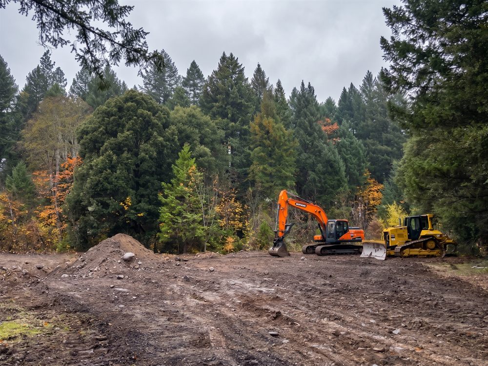 Excavator and dozer clearing forested land for a building site in Southern Oregon