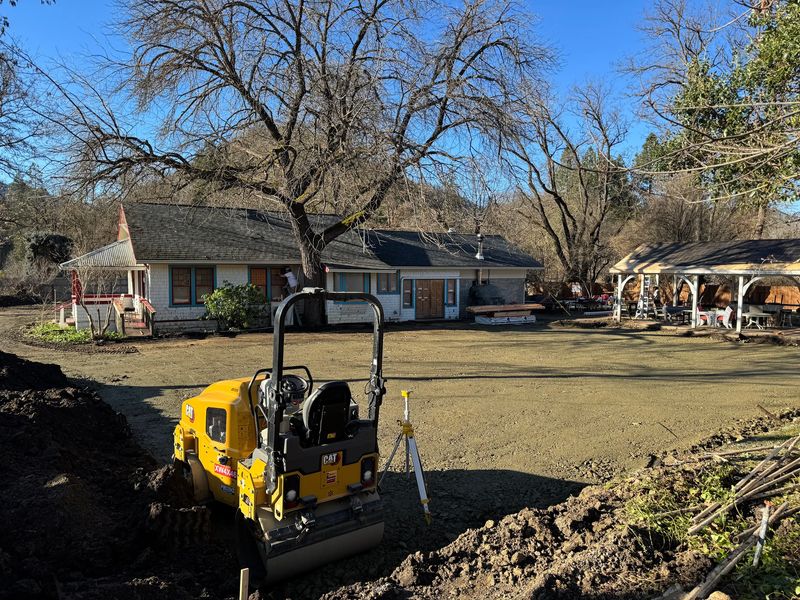CAT roller compacting the decomposed-granite base with survey equipment on site in Jacksonville, Oregon