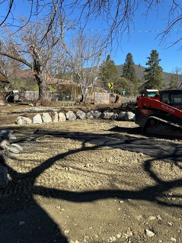 Skid steer setting a boulder border over filter fabric during site work in Jacksonville, Oregon