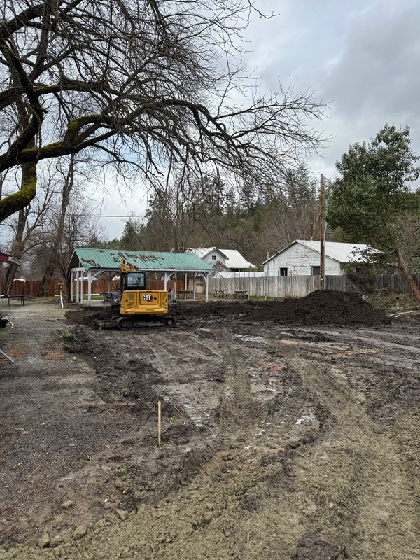 CAT excavator rough-grading the muddy commercial lot during site prep in Jacksonville, Oregon