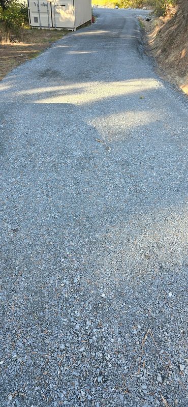 Freshly compacted gravel driveway leading to a property outbuilding with a graded drainage swale, Rogue Valley Oregon