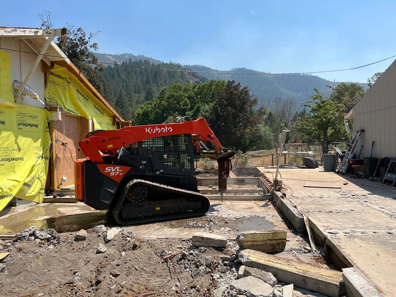 Skid steer with a hydraulic breaker removing old concrete during a custom home project in the Applegate, Oregon