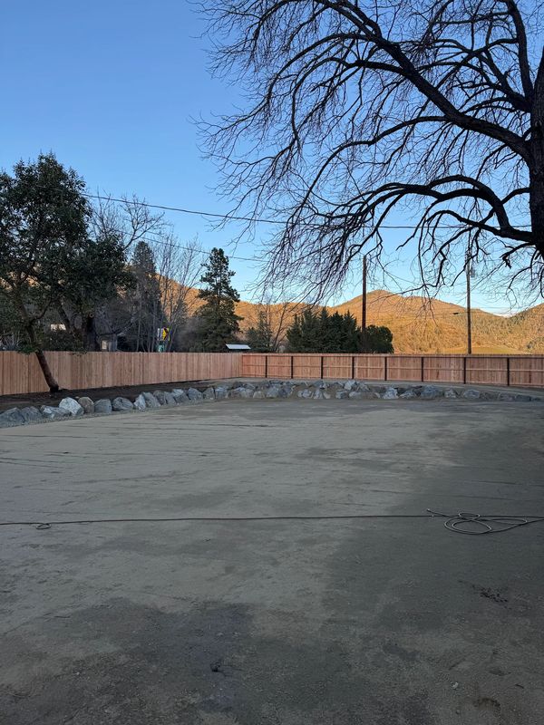 Finished decomposed-granite parking area with a curved rock border and new fence in Jacksonville, Oregon