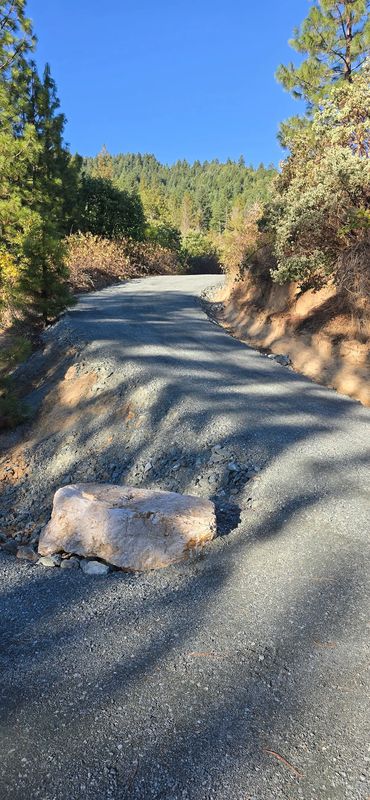 Newly rebuilt gravel driveway with a graded crown and drainage shoulder curving uphill through Southern Oregon forest