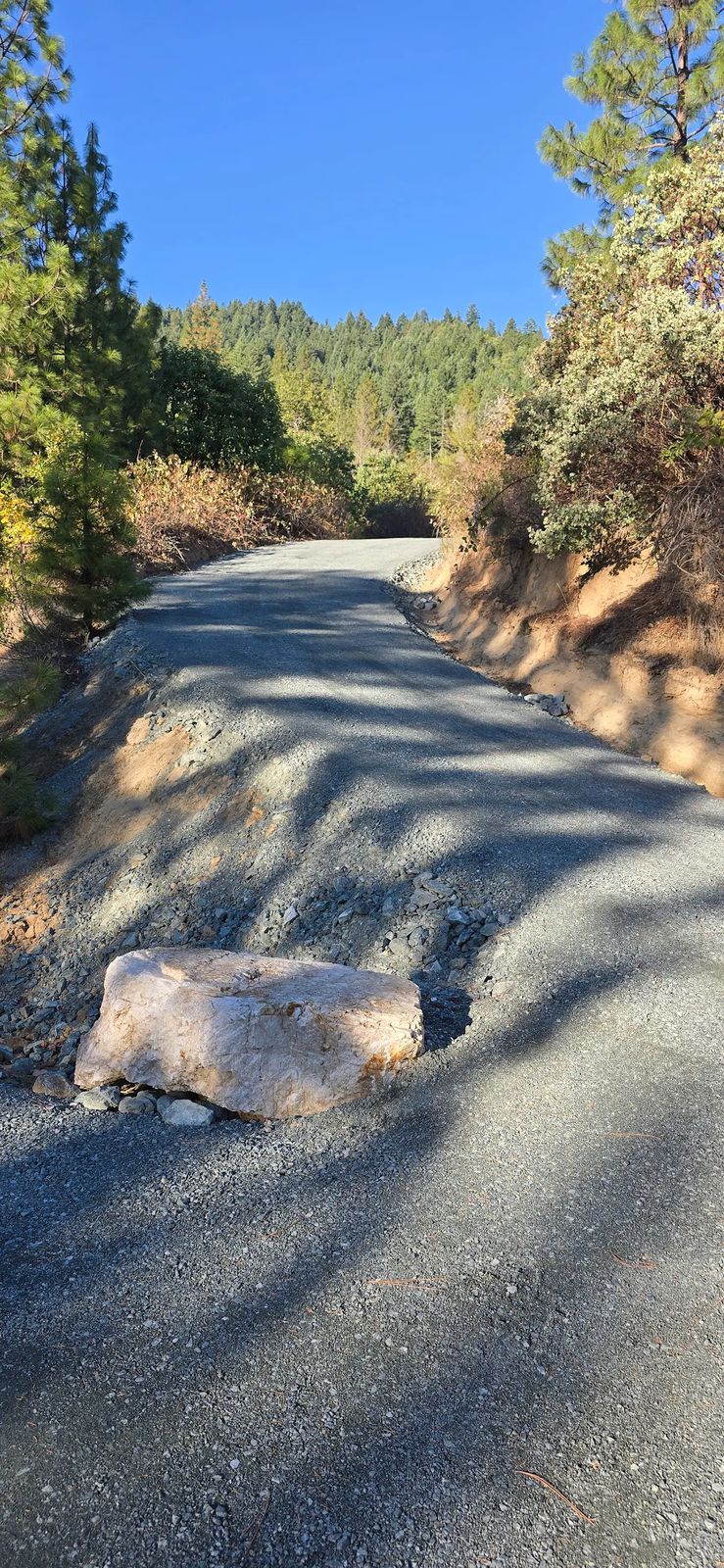Newly rebuilt gravel driveway with a graded crown and drainage shoulder curving uphill through Southern Oregon forest
