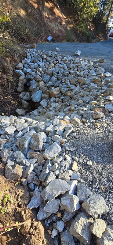 Rock-lined roadside drainage ditch and culvert channeling runoff away from a graded driveway, Rogue Valley Oregon