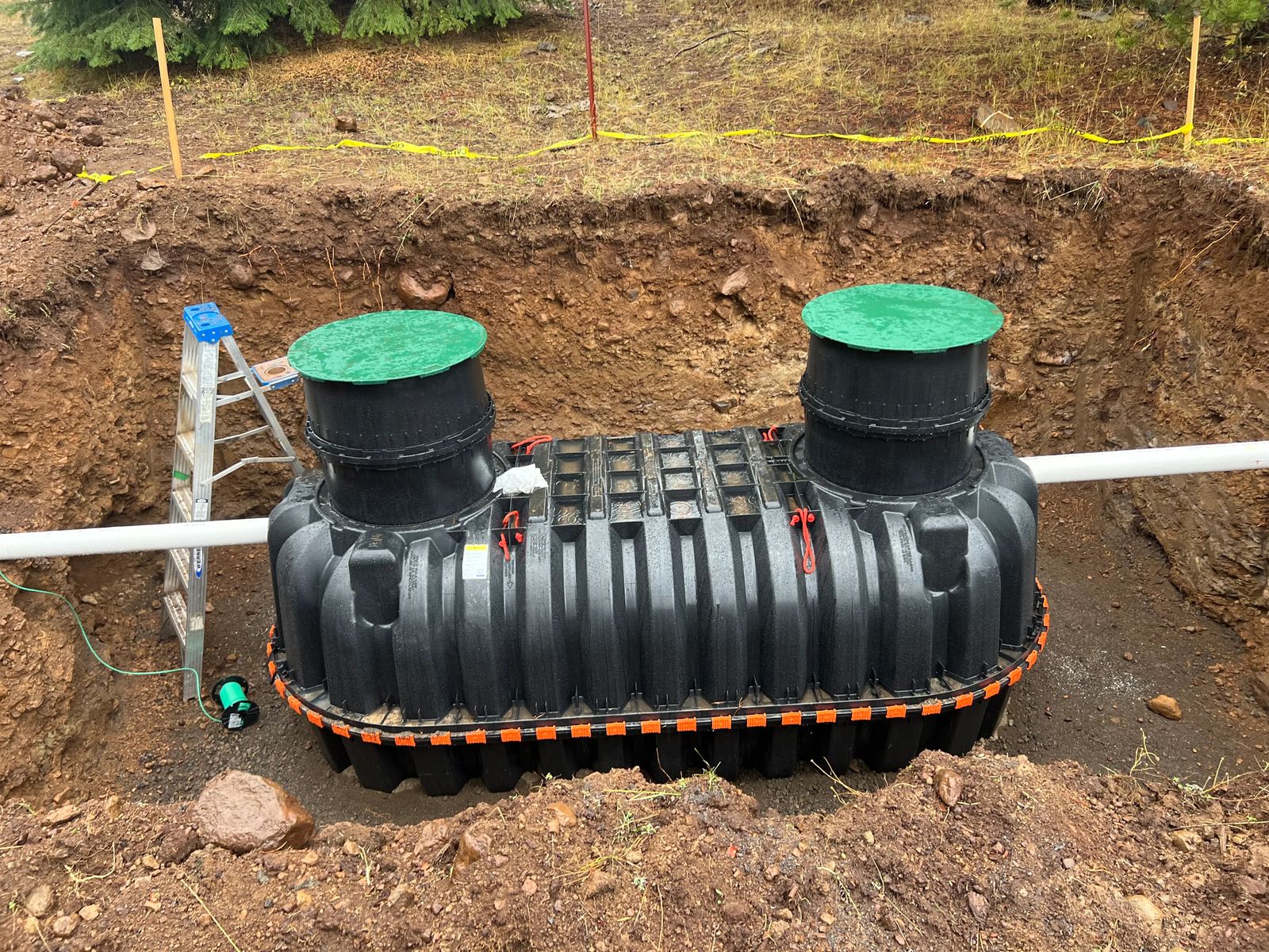 Septic tank with two access risers set in an excavated hole during installation on a high-elevation Southern Oregon property
