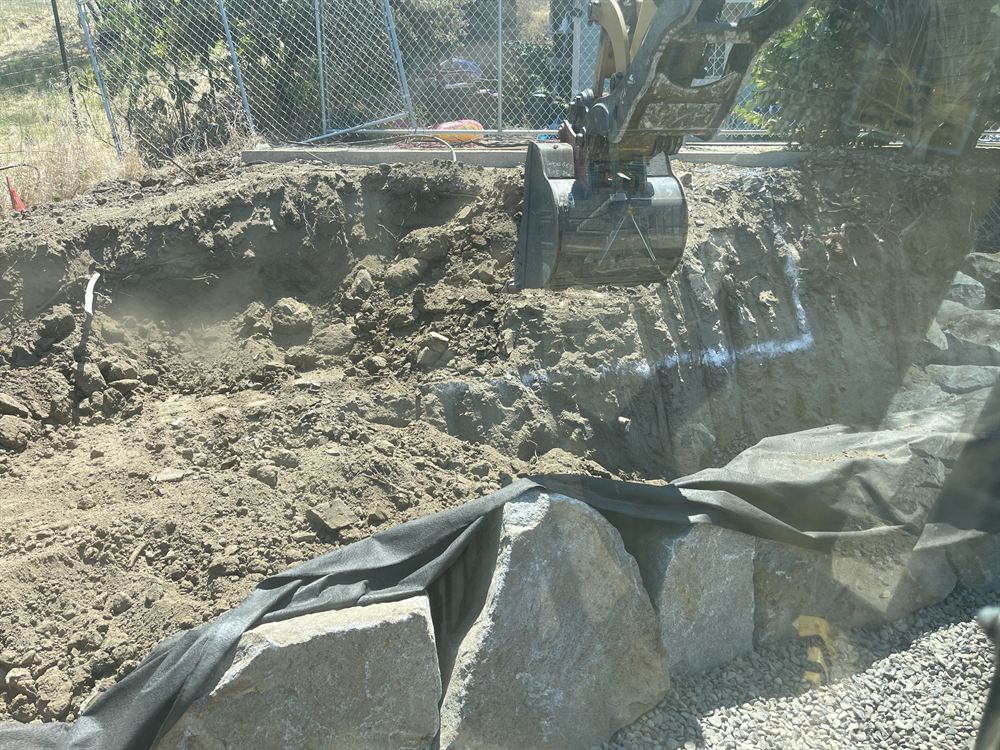 Excavator digging a large lined basin on a Southern Oregon property
